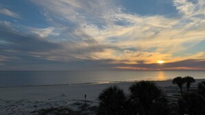 Una playa con un atardecer, palmeras y cielo despejado.