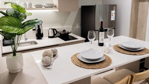 Una cucina moderna con piani di lavoro bianchi, un frigorifero in acciaio inossidabile e un'area pranzo con due piatti bianchi e bicchieri da vino.