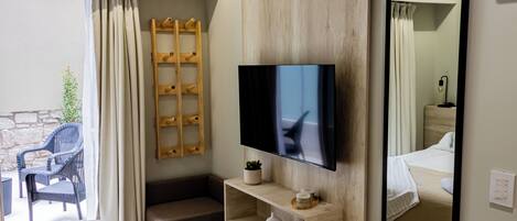 Una habitación de hotel moderna con una cama, un televisor montado en la pared, un estante de madera con artículos de aseo, un espejo y vistas al área de estar exterior.