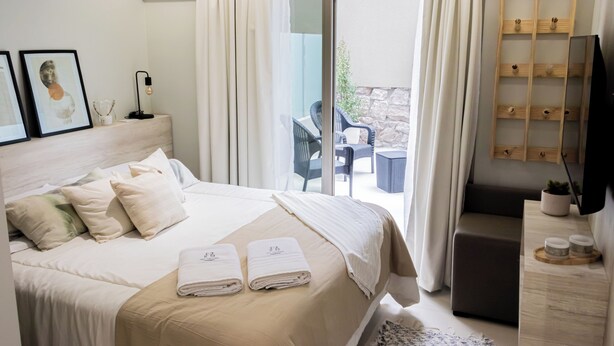 Una camera d'albergo moderna con un letto grande, una scrivania, una TV e un balcone con sedute all'aperto.