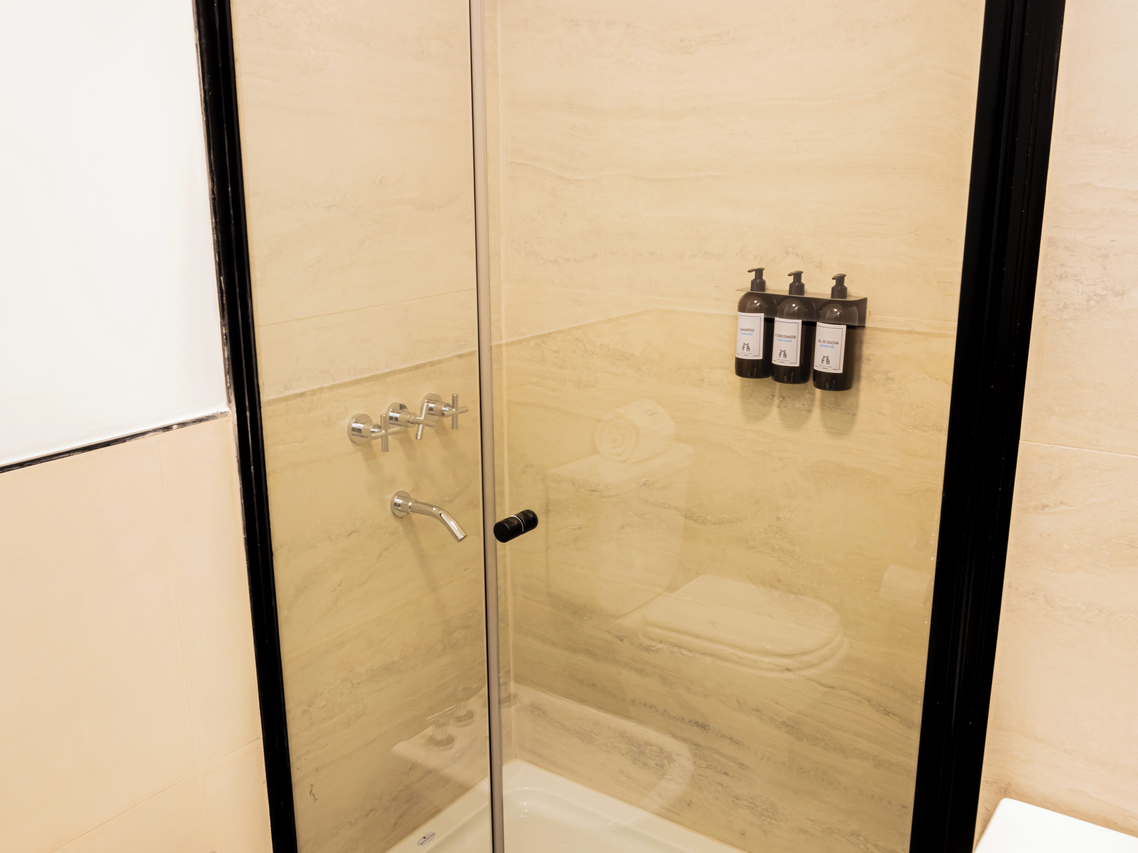 A glass-enclosed shower with a toilet and three bottles of shampoo.