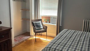 Une chambre à coucher comprenant un lit, une chaise, une armoire et une fenêtre avec des stores.