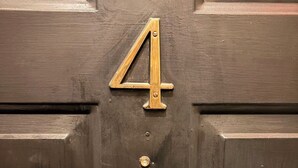 Une porte en bois sombre, ornée d’un numéro en laiton, le chiffre « 4 », qui indique le numéro de la maison.