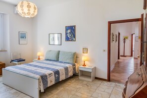 A bedroom with a bed, two bedside tables, a lamp, a wall-mounted artwork, and a hallway leading to another room.