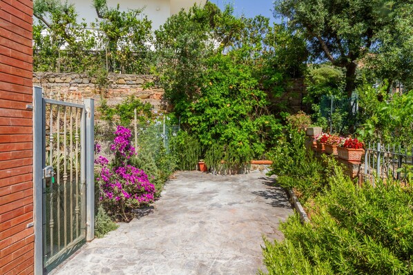 A stone pathway leading to a house with a brick wall and a metal gate.