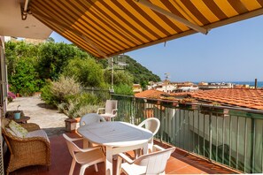 A terrace with a table and chairs, a covered area, and a view of the sea and buildings.