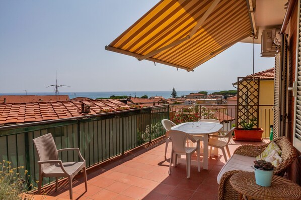 A terrace with a table and chairs, a potted plant, and a view of the sea.