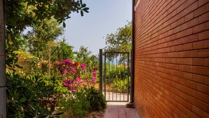 Un muro de ladrillo, una reja de metal y un sendero que lleva a un jardín con diversas plantas y flores.