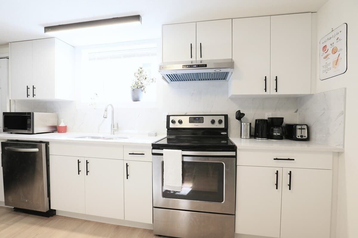 A modern kitchen with white cabinets, stainless steel appliances, a microwave, a dishwasher, a stove, and a coffee maker.