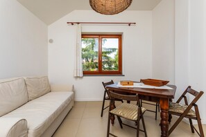 A room with a sofa, dining table, chairs, a window with a view, and a hanging basket.