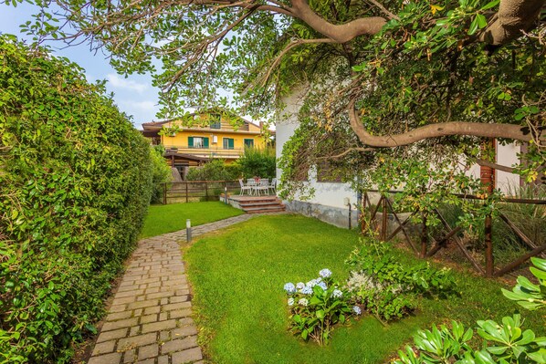 A garden with a paved path, a yellow building, and a white fence.