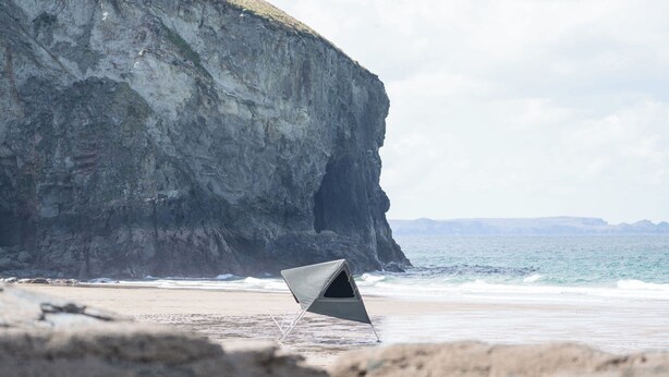 A beach with a tent set up on the sand near a cliff.