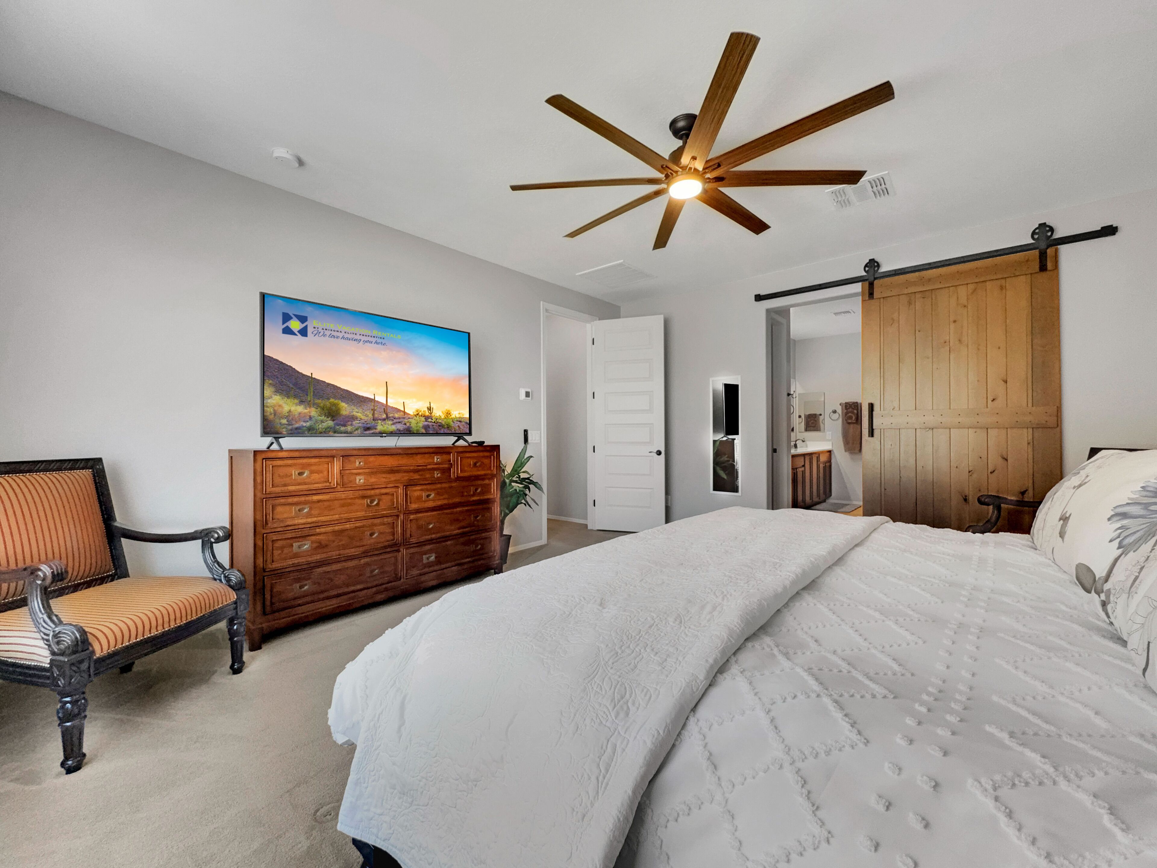A bedroom with a bed, a dresser, a television on the wall, and a ceiling fan.