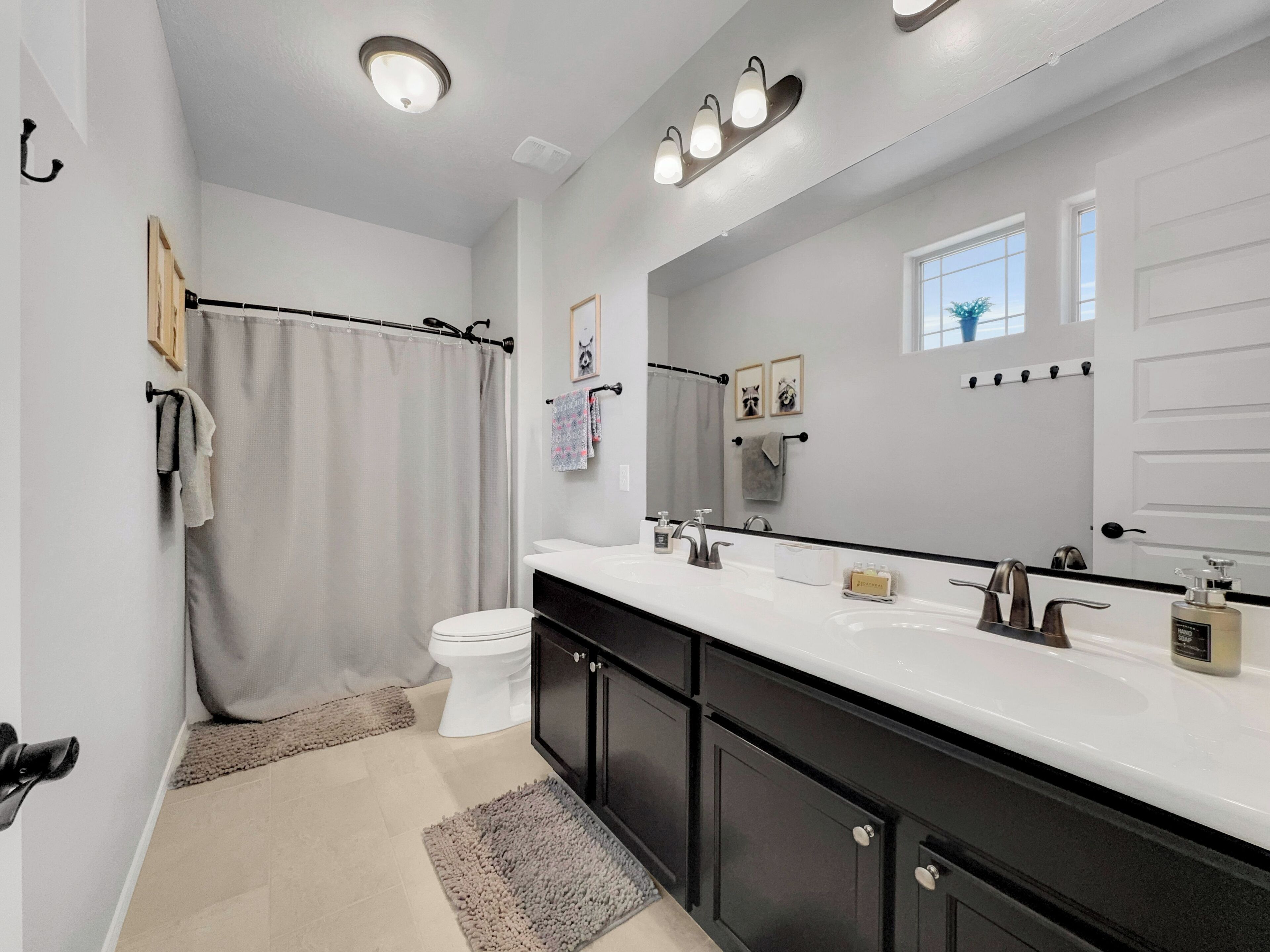 A modern bathroom with a white toilet, a large mirror, a black vanity, and a shower curtain.