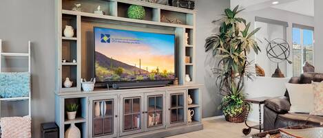 A living room with a flat-screen TV, a bookshelf, decorative items, and a large potted plant.