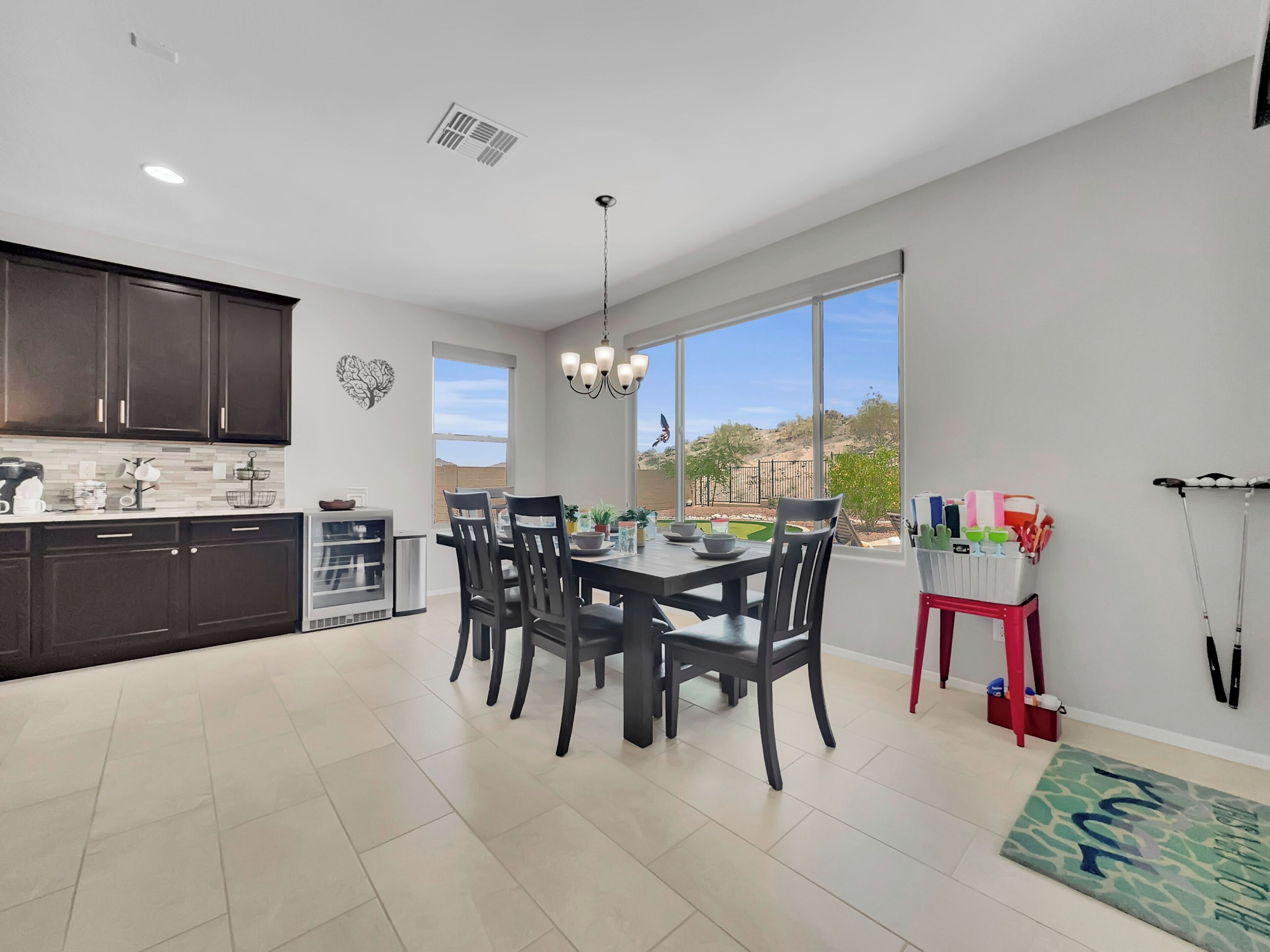 A modern kitchen with dark cabinets, a dining area with a large window, and a view of a landscaped yard.