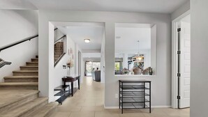 Un intérieur moderne avec un escalier, un couloir menant à une salle à manger et un coin bar doté d’une étagère.