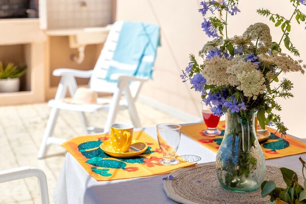 A table set with a vase of flowers, a yellow cup, and a glass on a tablecloth.