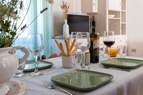 A dining table set with plates, glasses, a bottle of wine, and a vase with dried plants.