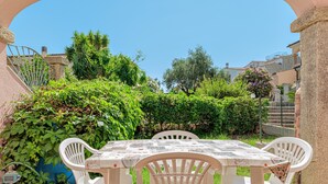 A patio with a table and chairs, surrounded by greenery and a stone wall. - Apartment 'Deledda' with Private Terrace, Private Garden and Air Conditioning (San Teodoro)