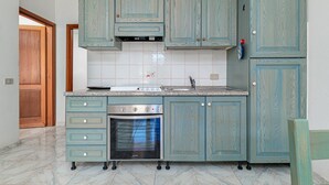 A kitchen with teal cabinetry, a built-in oven, and a stainless steel range. - Apartment 'Deledda' with Private Terrace, Private Garden and Air Conditioning (San Teodoro)