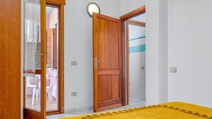 A room with a wooden door, a yellow rug, and a white wall. - Apartment 'Deledda' with Private Terrace, Private Garden and Air Conditioning (San Teodoro)