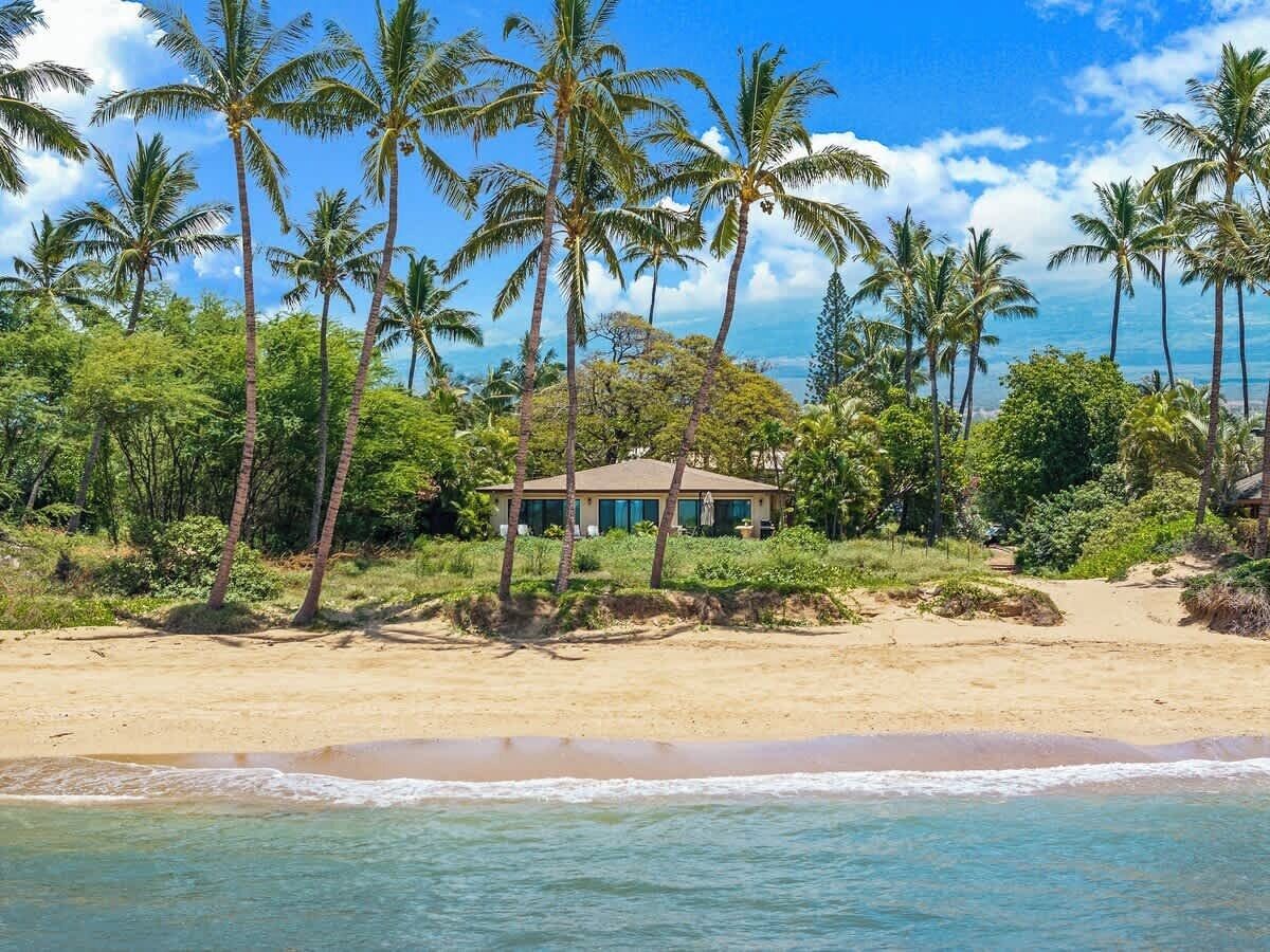 A beachfront property with a house surrounded by palm trees and a sandy beach.