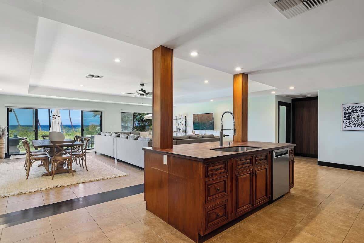 A modern kitchen with a large island, wooden cabinets, and a view of the ocean.