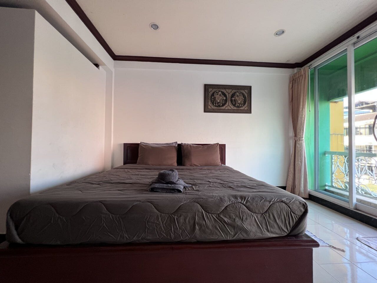 A hotel room with a large bed, a headboard, a window with a view, and a wall-mounted picture.