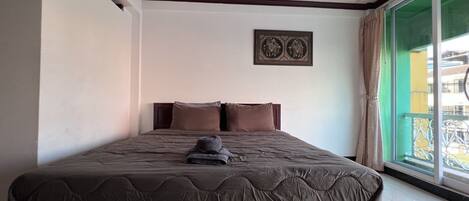 A hotel room with a large bed, a headboard, a window with a view, and a wall-mounted picture.