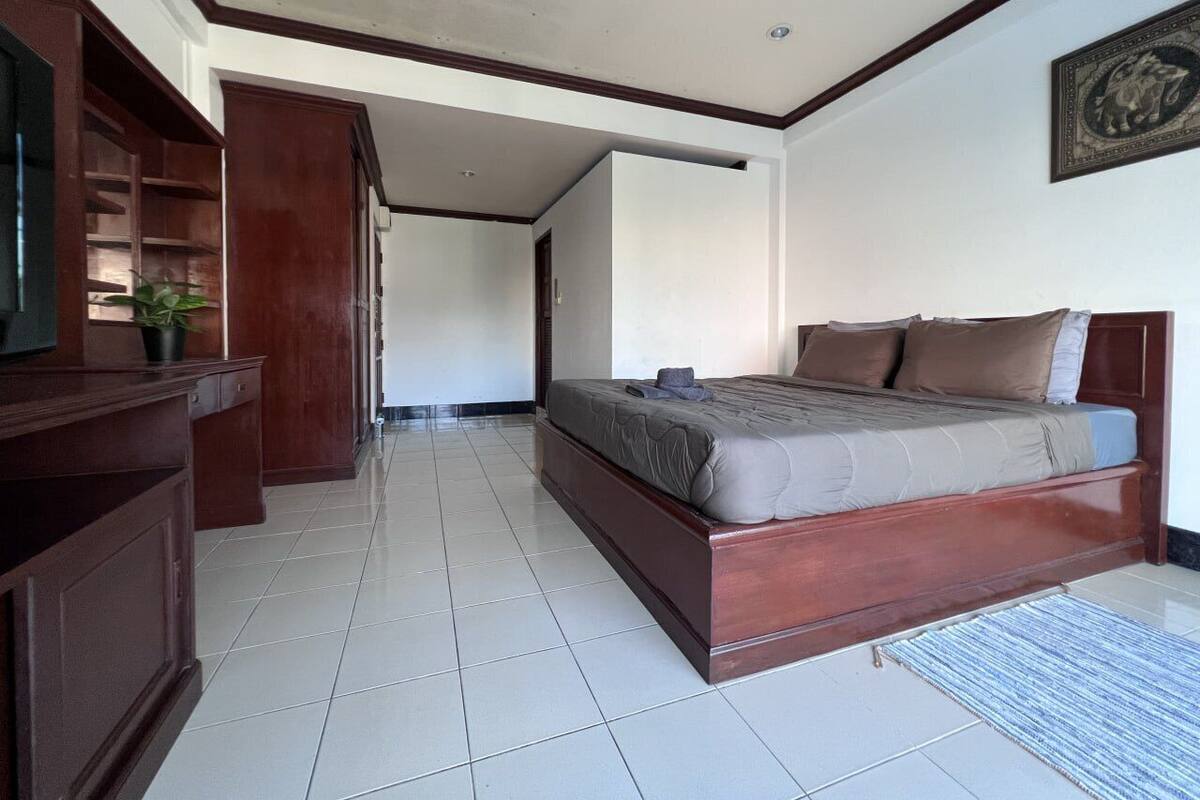 A bedroom with a wooden bed, a desk with a plant, and a tiled floor.