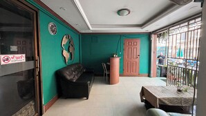 A room with a green wall, a black leather sofa, a wooden door, and a small table with a plant. - Green Hotel (Pattaya)