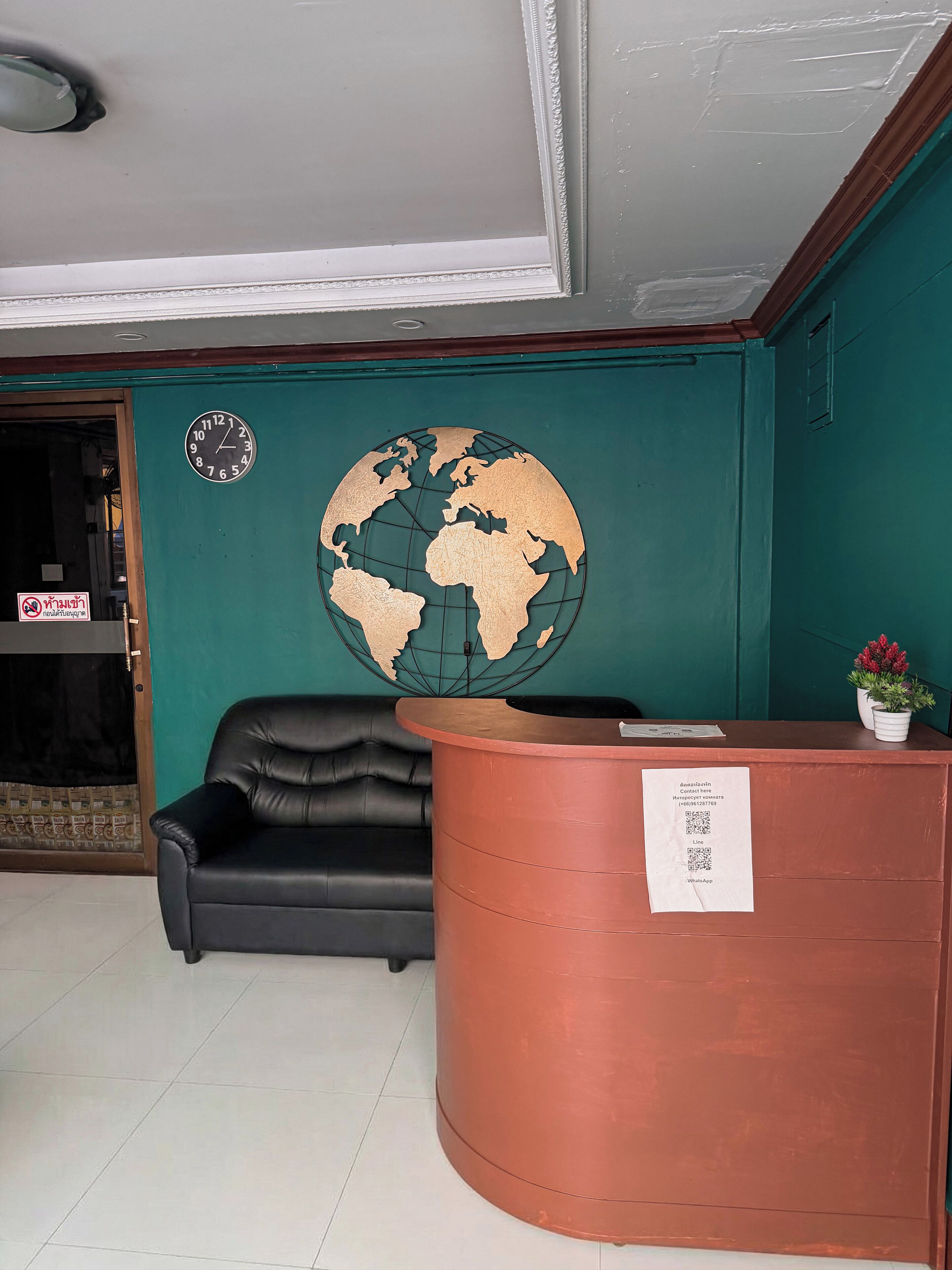 Een receptiegedeelte met een zwarte leren bank, een koperkleurig receptiebalie, een globe aan de muur en een deur met een bordje.