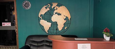 A reception area with a black leather couch, a copper-colored reception desk, a wall-mounted globe, and a door with a sign.