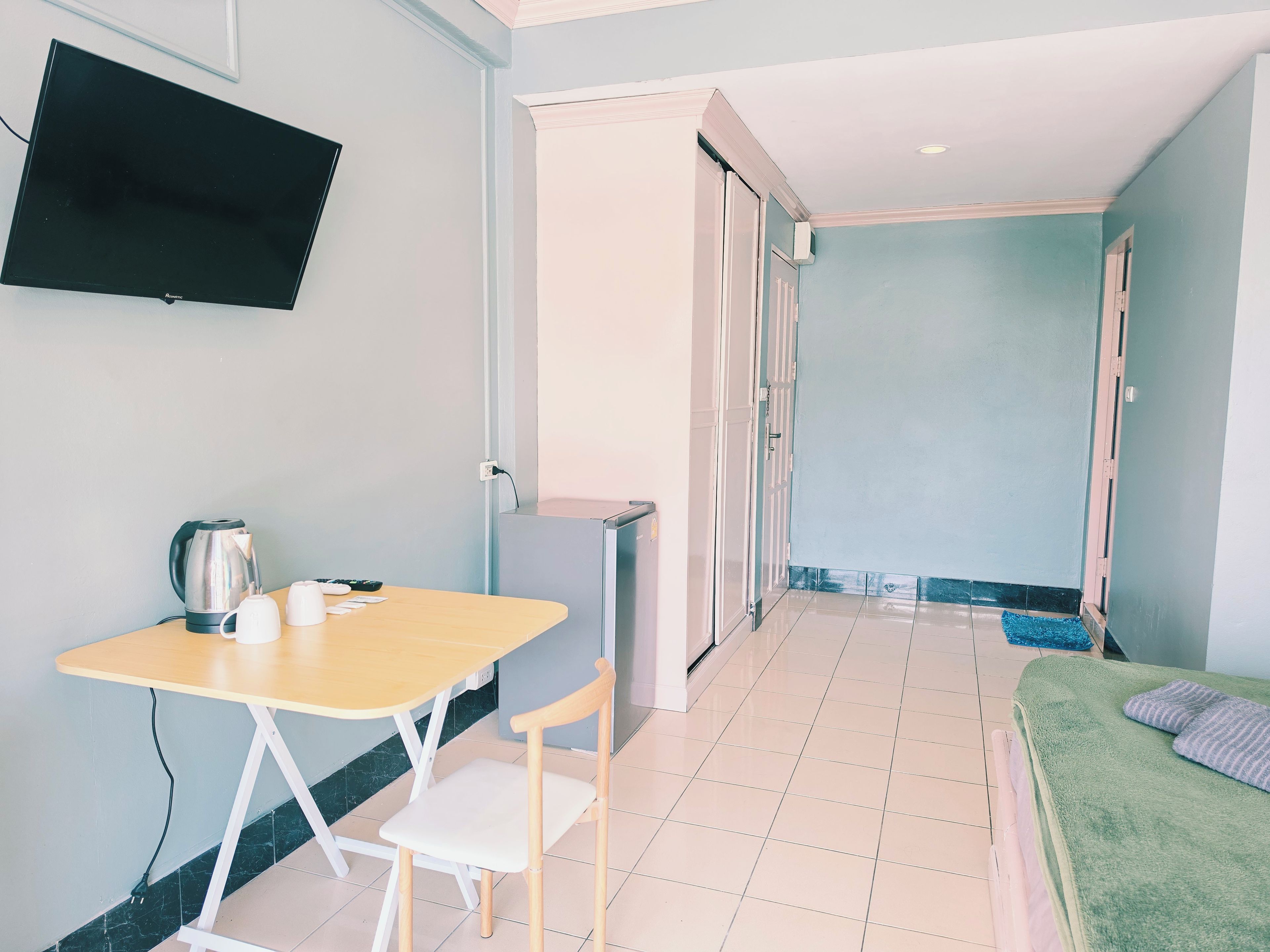 A room with a bed, a table with chairs, a television, and a kitchenette area.