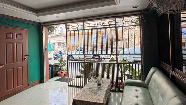 A spacious living area with a sofa, a coffee table, and a view through a barred window. - Green Hotel (Pattaya)