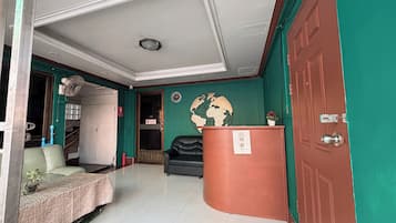 Eine Hotellobby mit grüner Wand, einer schwarzen Leder-Couch, einem Holzbüro und einer Globen-Dekoration.
