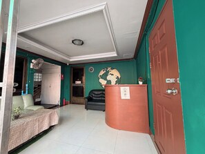 A hotel lobby with a green wall, a black leather sofa, a wooden reception desk, and a globe decoration. - Green Hotel (Pattaya)