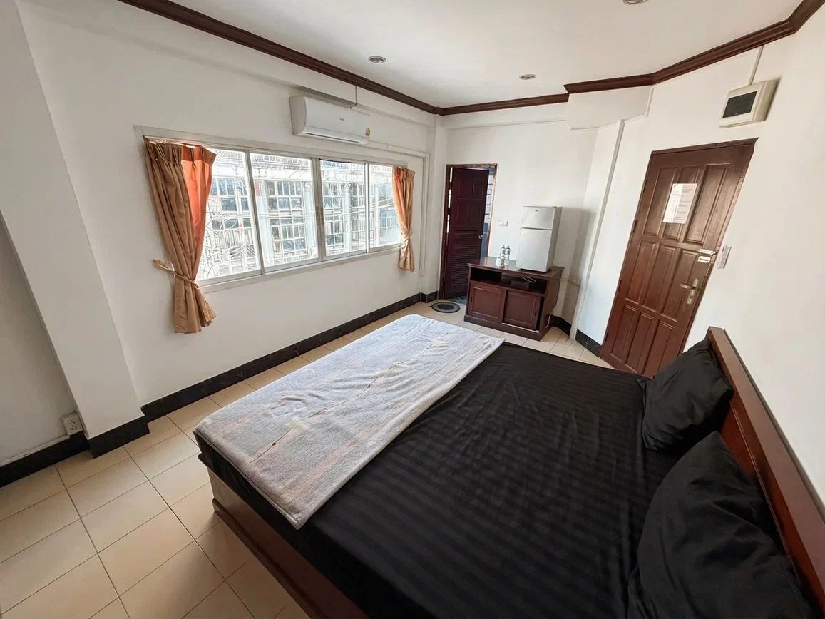 A hotel room with a bed, a desk, a chair, a window with curtains, and a door.