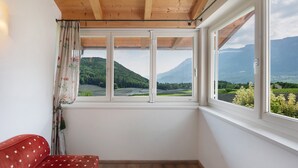A room with a wooden ceiling, a red sofa, and a view of a mountainous landscape through large windows. - Holiday Apartment 'Schwalbennest' with Mountain View, Wi-Fi and Air Conditioning (Appiano sulla Strada del Vino)