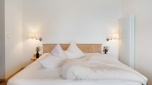 A neatly made bed with pillows, a wooden headboard, bedside lamps, and a radiator. - Holiday Apartment 'Schwalbennest' with Mountain View, Wi-Fi and Air Conditioning (Appiano sulla Strada del Vino)