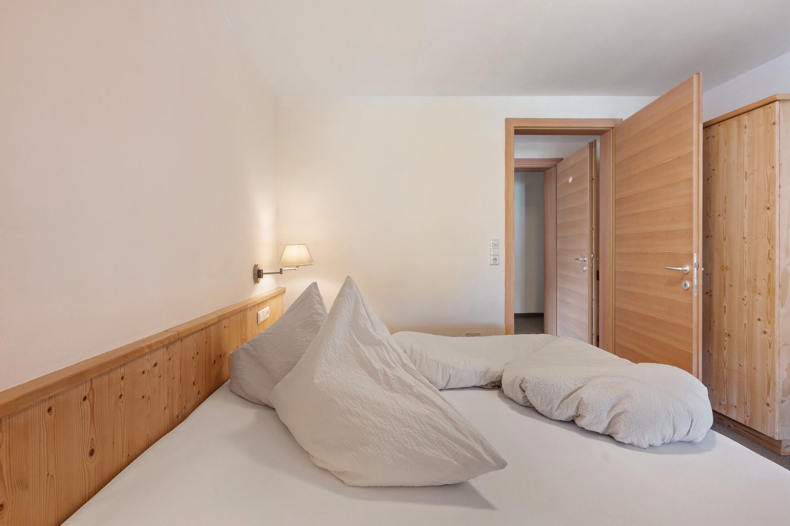 Ein Schlafzimmer mit einem hölzernen Kopfteil, einem Bett mit weißer Bettwäsche, einer Nachttischlampe und einem Holzschrank.