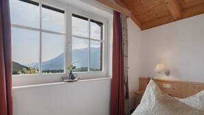 A bedroom with a large window, wooden ceiling, and a bedside lamp.