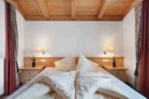 Ein Schlafzimmer mit Holzboden, einem Bett mit weißer Bettwäsche, zwei Nachttischlampen und blumigen Vorhängen.