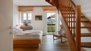 Un dormitorio con cama de madera, una silla, un ventanal y una escalera de madera.