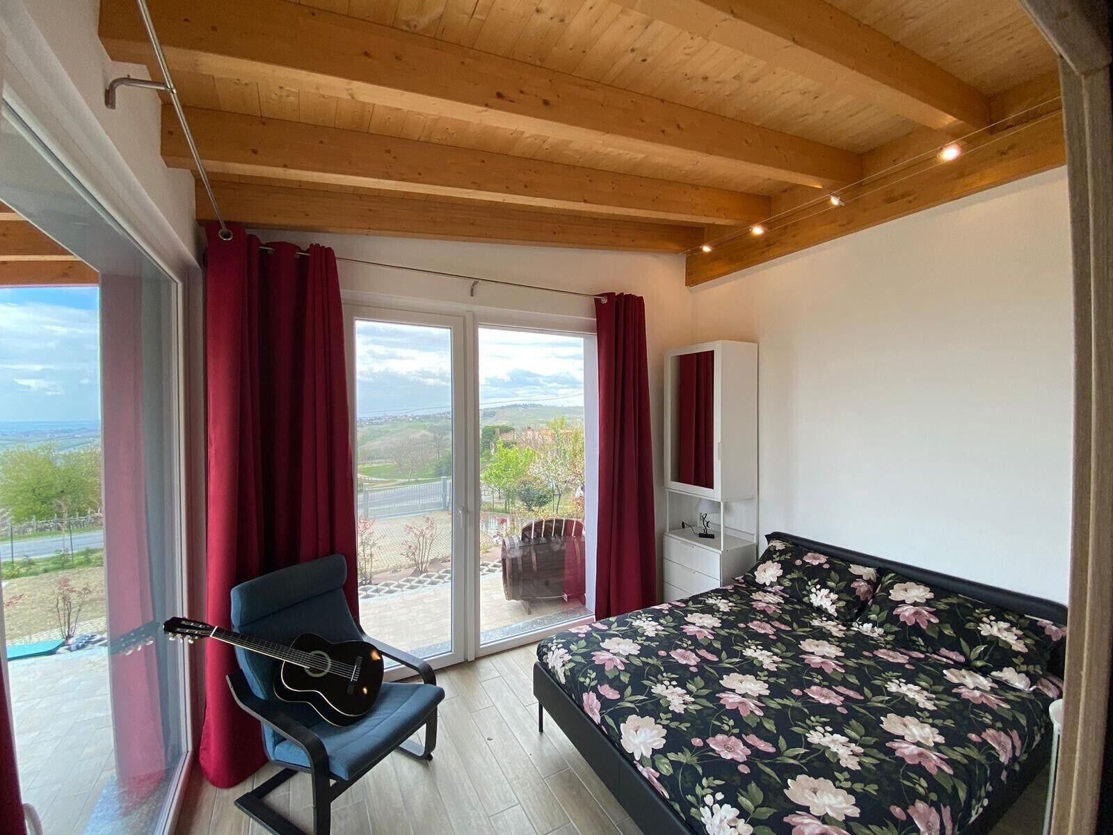 Ein Schlafzimmer mit Bett, Stuhl, Gitarre, Kleiderschrank und einem Balkon mit Blick.