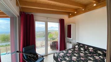 Ein Schlafzimmer mit Bett, Stuhl, Gitarre, Kleiderschrank und einem Balkon mit Blick.