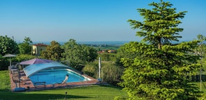 A swimming pool with a covered area, surrounded by greenery and a view of distant buildings.