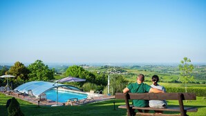 A couple sitting on a bench overlooking a swimming pool with a view of a vineyard and distant town. - Villa 'Casa Vacanze Elios B' with Mountain View, Wi-Fi and Air Conditioning (Unknown)