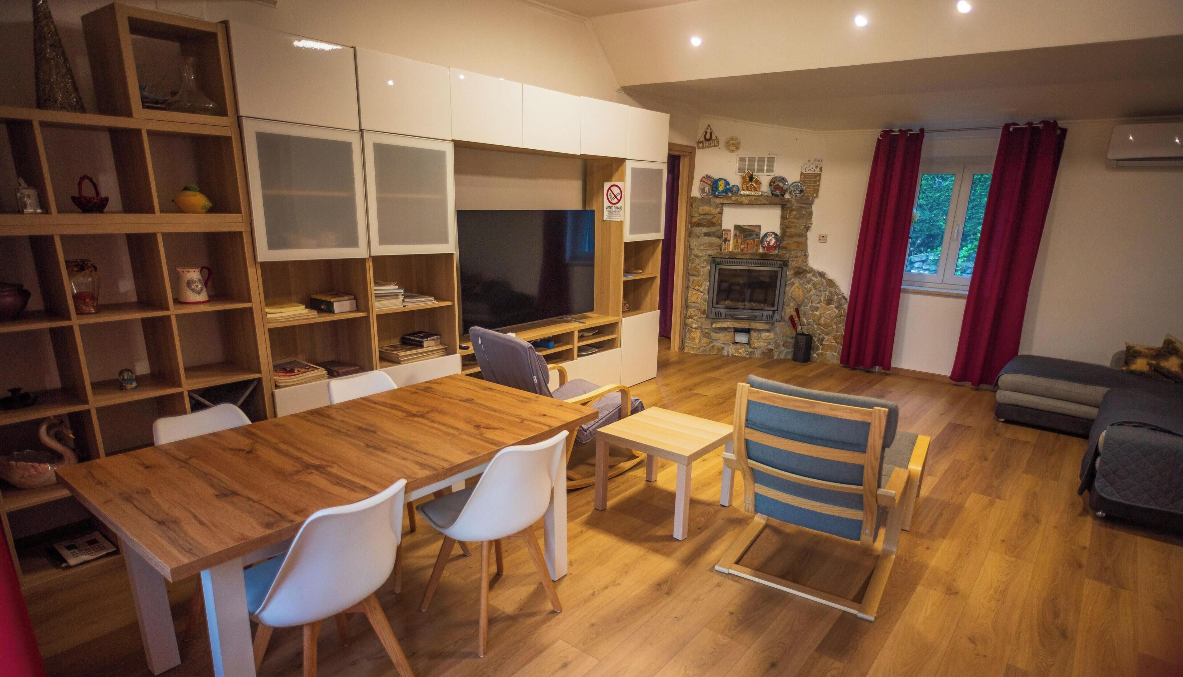 Een moderne woonkamer met een houten eettafel, witte stoelen, een televisie en een open haard.